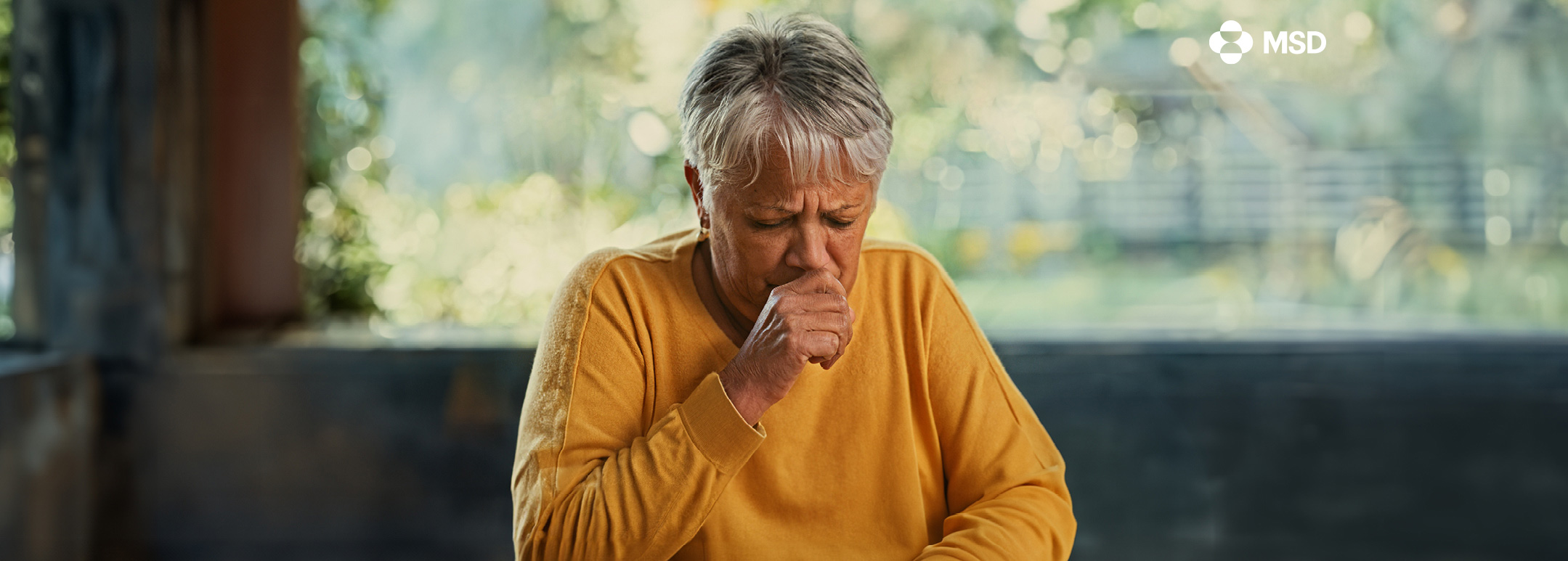 A concerned older woman coughs into her hand.